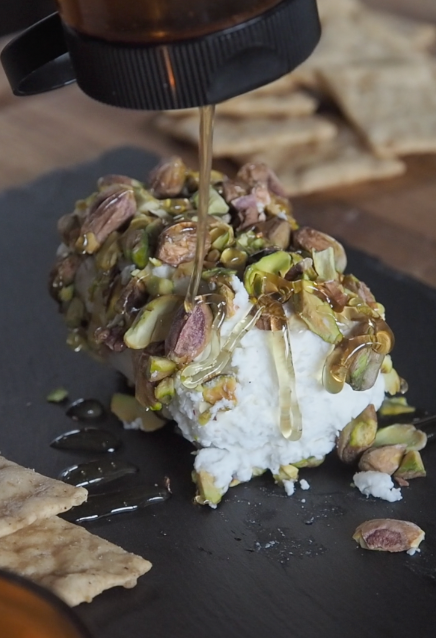 Goat cheese log rolled in pistachio chunks & drizzle of Bee Mafia Hot Honey on top.