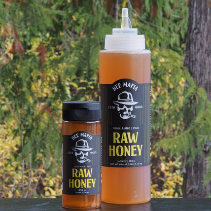 Bee Mafia Combination of 350 gram bottle of raw honey and larger 40 oz raw honey chef sqeeze bottle with trees in background.