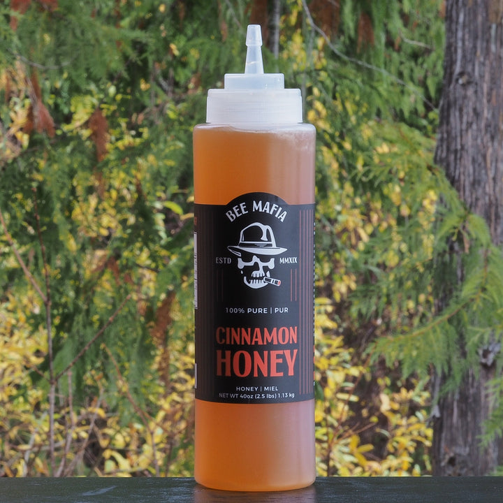 Bee Mafia Honey infused with Cinnamon in a 40 fl oz chef bottle with treets in the background.