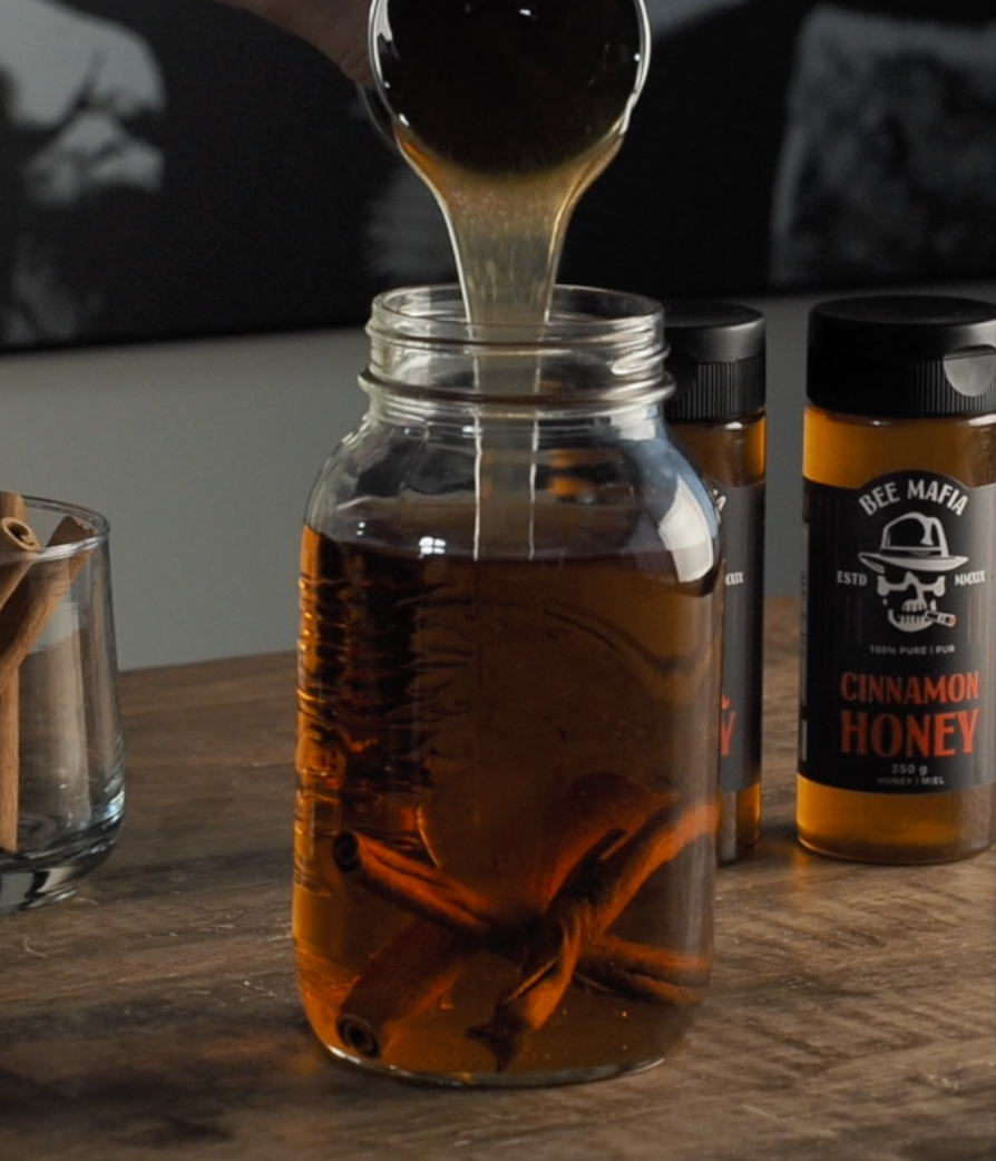 Honey being poured into a mason jar of whiskey that is to become a hot cinnamo honey whiskey drink.