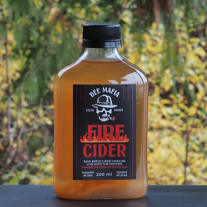 Bottle of Fire Cider with Trees in the background of Bee Mafia Fire Cider Canada.